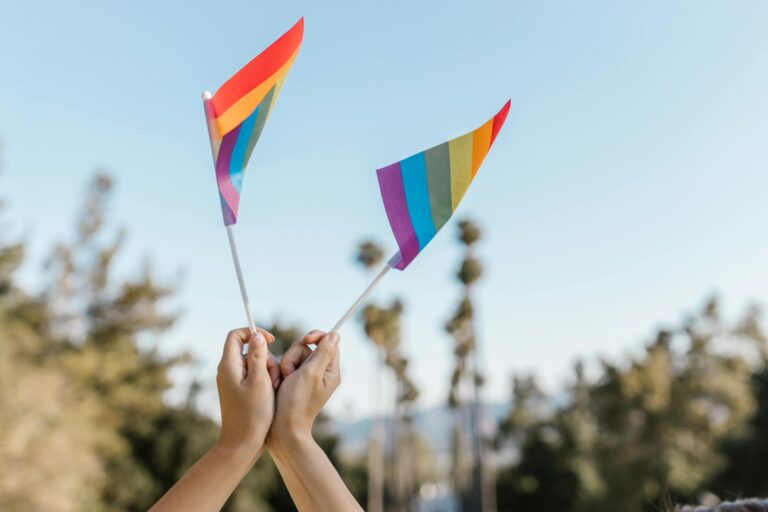 Hands holding rainbow flags outdoors, symbolizing pride and diversity.
